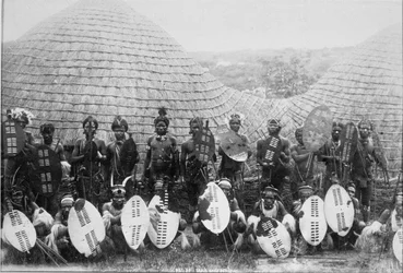 Ritratto di gruppo di guerrieri Zulu fuori da una capanna, c.1875
